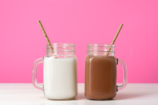 Glass jars with flavoured milkshakes against pink background close up