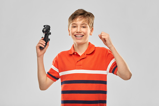 childhood, fashion and people concept - portrait of happy smiling boy in red polo t-shirt with gamepad playing video game over grey background