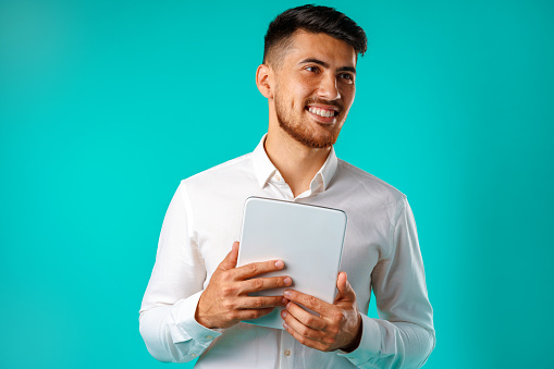 Young businessman wearing white shirt holds digital tablet against green background