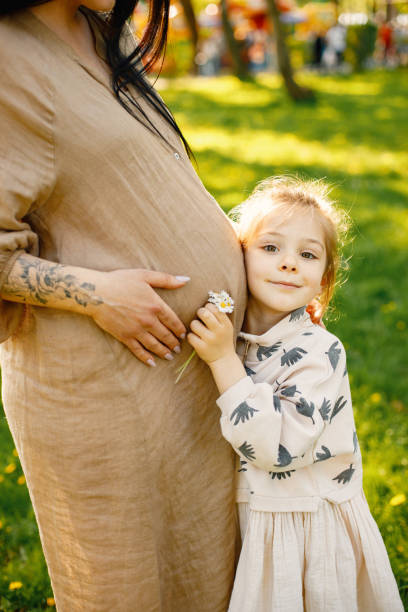 Cropped photo of a little girl hugging pregnant belly of mother in park stock photo