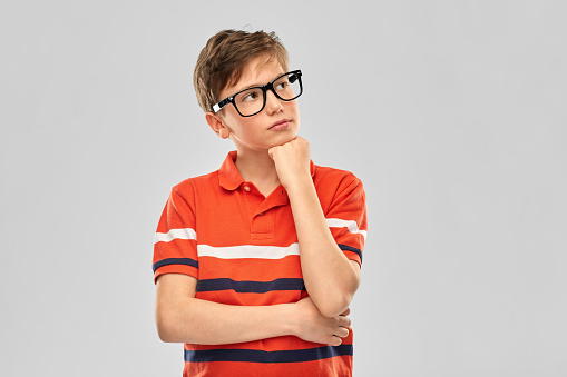 vision, education and school concept - portrait of thinking boy in eyeglasses and red polo t-shirt over grey background