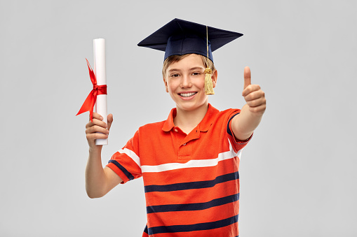 school, education and graduation concept - portrait of happy smiling graduate student boy in bachelor hat or mortarboard with diploma over grey background