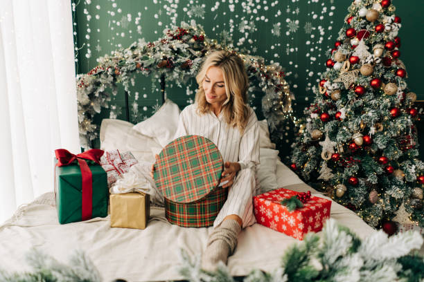 istock Attractive woman sitting on the bed in christmas opens gift boxes 1410290942