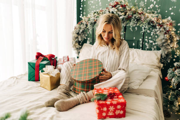 istock Attractive happy woman sitting on bed in christmas time opens gift boxes 1410290947