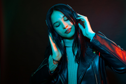 Studio portrait of an attractive 18 year old woman with long black hair with wireless headphones listening to music