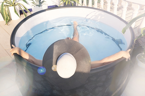 a woman in a hat bathes in a small mini-pool with a hot tub with blue water on the roof of the house in the sun against the backdrop of tropical plants, top view, selective focus