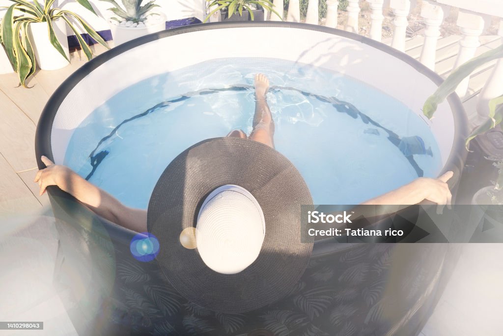 a woman in a hat bathes in a small mini-pool with a hot tub with blue water on the roof of the house in the sun against the backdrop of tropical plants, top view, selective focus a woman in a hat bathes in a small mini-pool with a hot tub with blue water on the roof of the house in the sun against the backdrop of tropical plants, top view, selective focus. Hot Tub Stock Photo