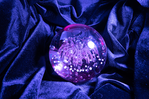 This is a photograph of a crystal ball made from green and purple fluorite on a white marble table top background.