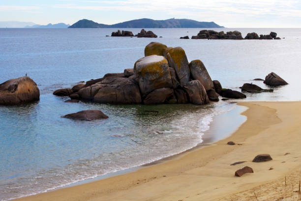 Ons islands silhouette seen from O Grove peninsula at dusk. This island belongs to  Islas Atlánticas National Park. Rías Baixas, Pontevedra province, Galicia, Spain. Beach and rock formations in the foreground.