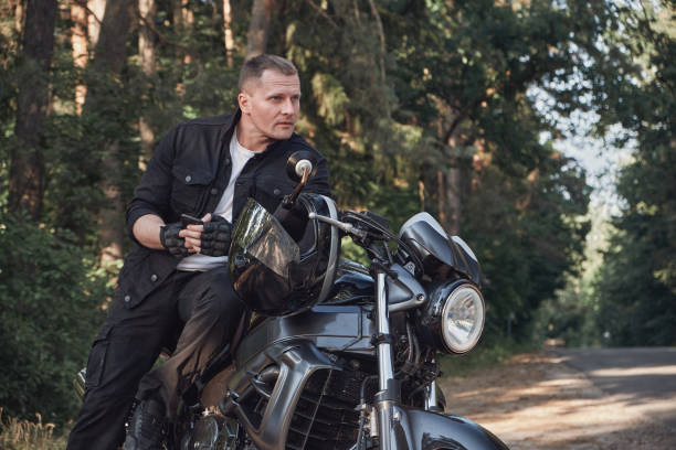 istock Young male biker travels on a motorcycle alone, stopped and using a mobile phone on the side of a forest road 1410299806