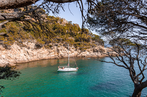 Coastal landscape with rocky hills and trees. Boat or yacht sailing on the shore on Costa Brava in Spain