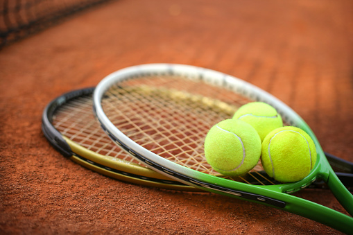 Two tennis rackets and three tennis balls on a clay court.