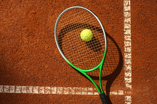 Tennis racket and a tennis ball on a clay court.