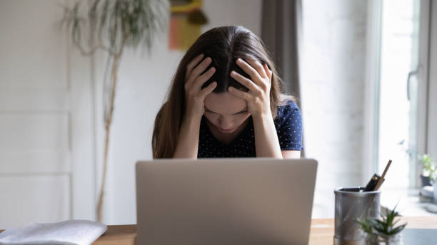 istock Frustrated unhappy laptop user girl touching head at work table 1410302524