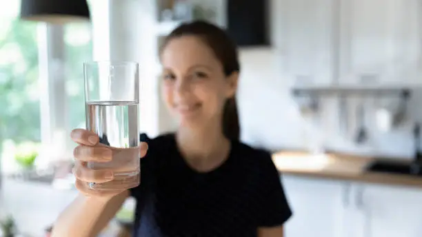 Photo of Happy young woman drinking clean mineral water in home kitchen