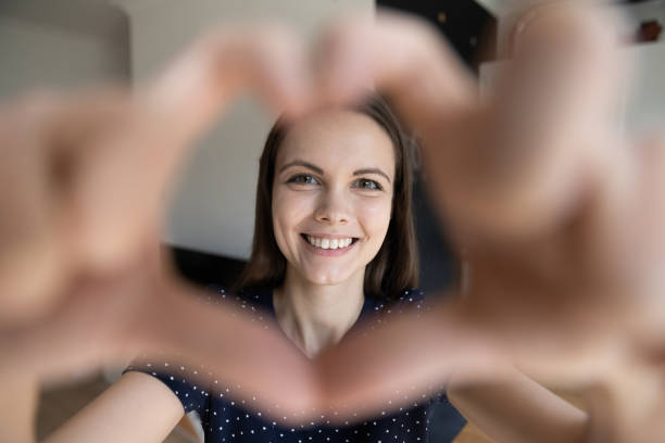 istock Happy pretty young woman smiling through hand heart shaped frame 1410302779