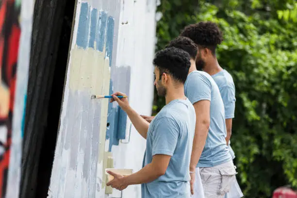 Photo of Young adults stand near each other as they paint