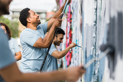 The group of coworkers smile while they help paint the graffiti wall.