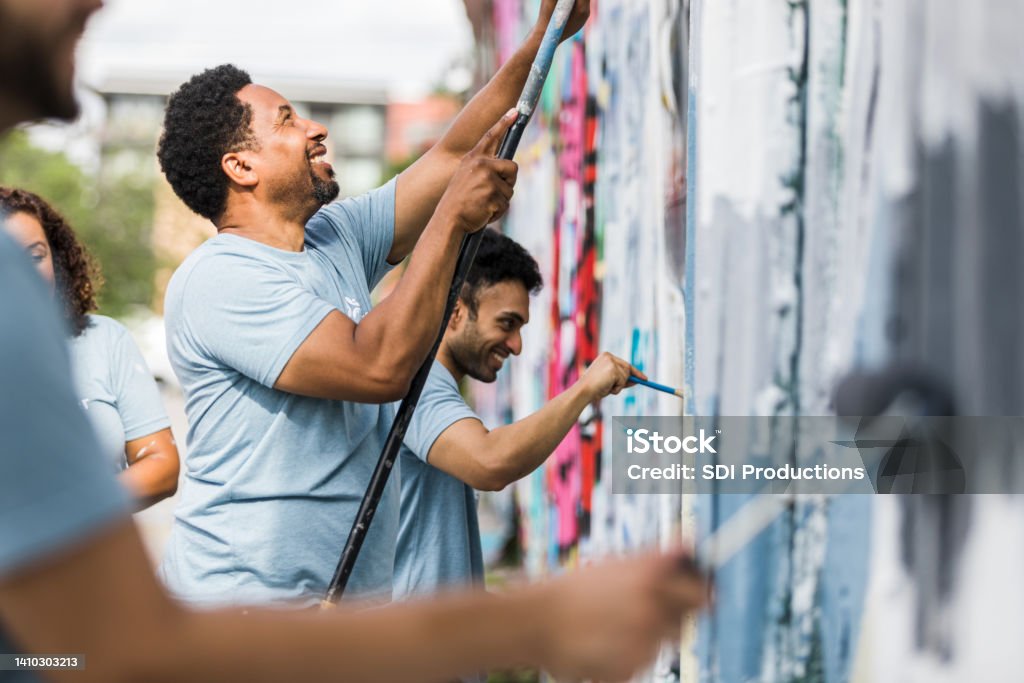 Coworkers smiling while they paint The group of coworkers smile while they help paint the graffiti wall. Volunteer Stock Photo