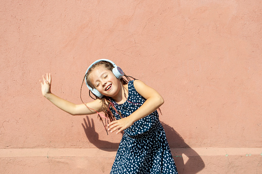 Cute little girl listening to music and dancing wearing headphones. Blurred dancing girl.