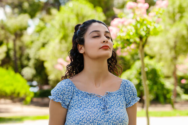 Young caucasian woman wearing a blue floral summer dress standing on city park, outdoors breathing fresh air. Concept of healthy lifestyle. stock photo