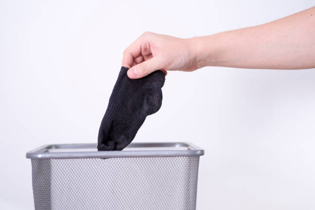 istock A man is throwing an old sock into a trash can with his hand against a white background. 1410317051