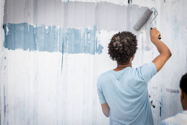 Unrecognizable young man uses roller to paint metal wall