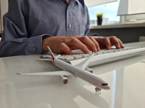 White model of airplane and persons on laptop keyboard. Introduction to global aviation related things can be done online at hand, ticket booking flight schedule tracking, shipping