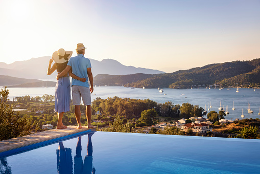 Loving couple on vacation time enjoys the summer sunset over the Aegean Sea by the swimming pool, Poros island, Greece
