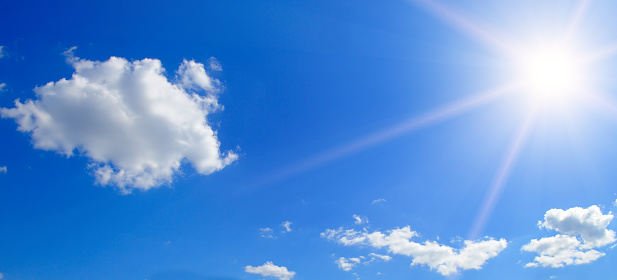Sunny background, blue sky with white clouds and sun. Wide photo.