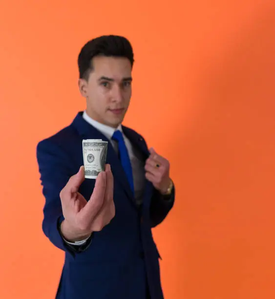 Photo of shot of a wad of bills being holding by a dapper man dressed in suit