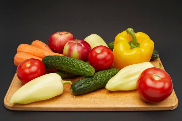 Group of vegetables and fruits on wooden cutting board isolated on black background.