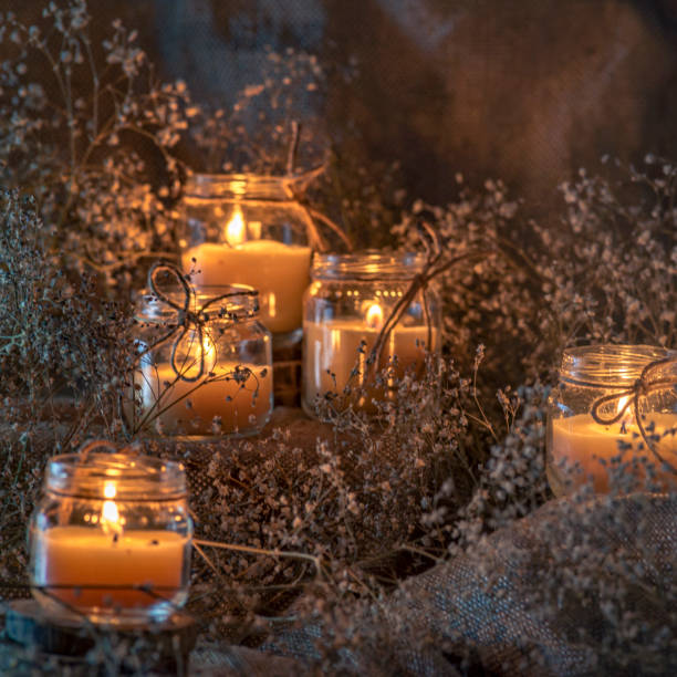 istock Wax handmade home-based  Burning white candle in the jar coarse textile Vintage  glow Flame dry bouquet gypsophila flower rustic dark mood orange blue light 1410334657