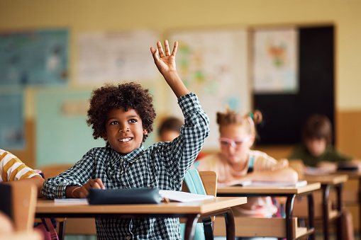 Happy African American schoolboy raising arm to answer a question in the classroom.