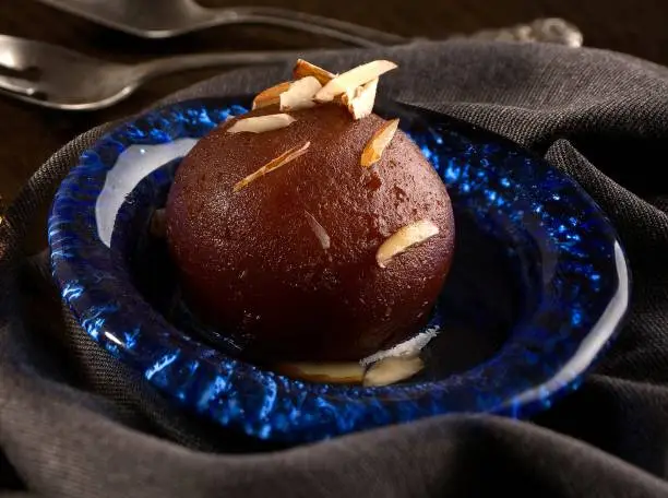 Photo of Indian sweet Gulab jamun garnished with almond and pistachio served in a dish isolated on dark background side view