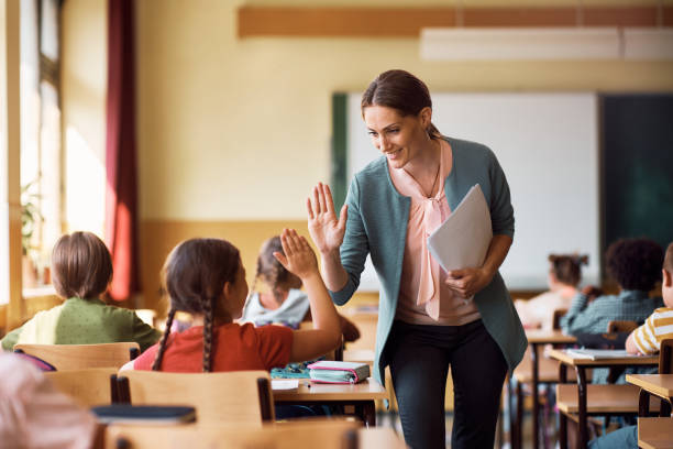 happy teacher and schoolgirl giving high five during class at school. - 學生 圖片 個照片及圖片檔