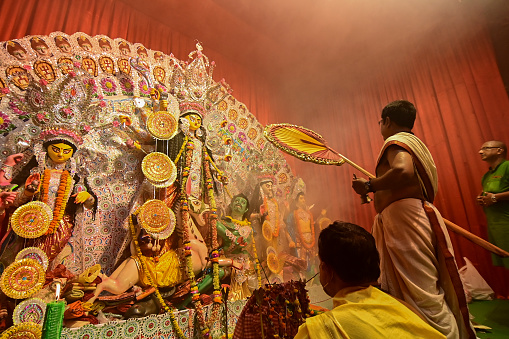 Howrah, India -October 13, 2021 : Hindu Priest worshipping Goddess Durga with ghanta and hand fan. Ashtami puja aarati - sacred Durga Puja ritual - shot at night.