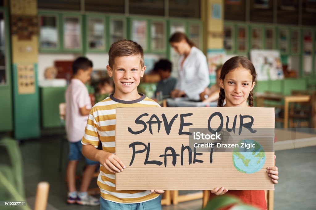 Let's save the planet for future generations! Happy elementary students holding placard with 'save our planet' message in the classroom and looking at camera. Education Stock Photo