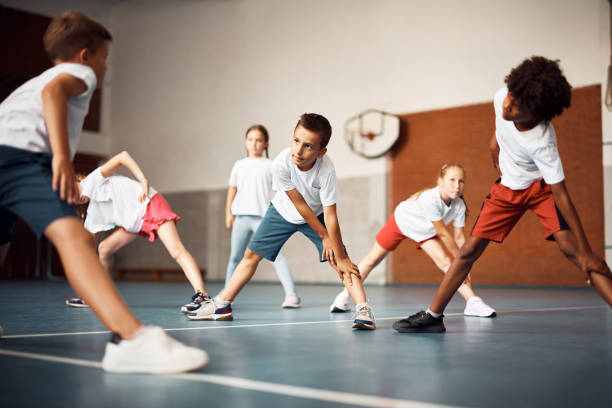 Elementary students stretching while warming up during physical education class at school gym Multiracial group of school kids stretching during PE class at school gym physical education stock pictures, royalty-free photos & images