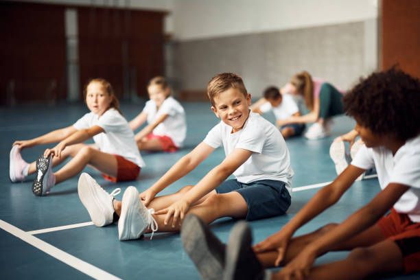 istock Happy schoolboy talking to his friend while doing stretching exercises on PE class. 1410337911