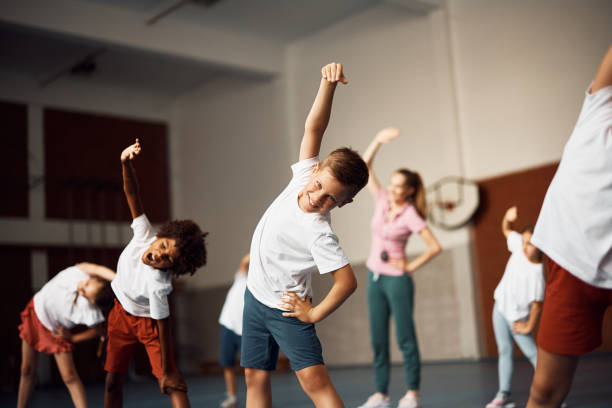 istock Happy schoolboy doing stretching exercise during physical education class at school gym and looking at camera. 1410337951