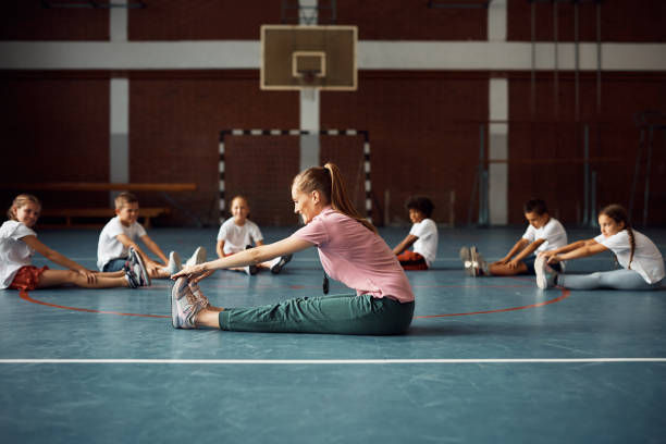 istock Happy coach and group of elementary students doing stretching exercises on PE class at school gym. 1410338017