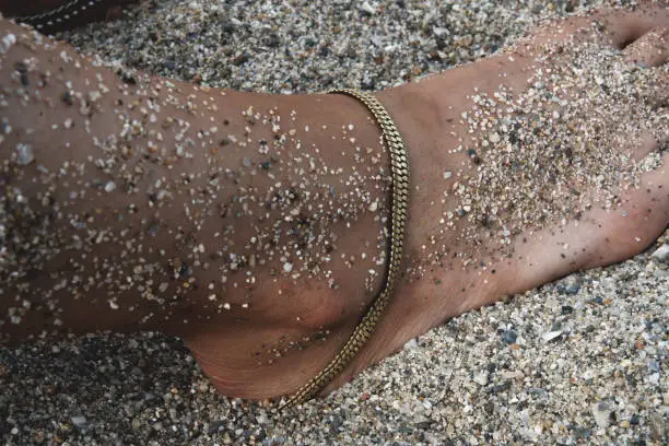 Foot of a woman in the sand wearing a foot bracelet