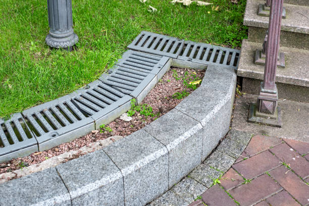 iron drainage grate on the roadside with green grass and stone pebbles at the granite curb along the pedestrian pavement of stone tiles near stairs with steps on city park, nobody. rejilla de drenaje de hierro en el borde de la carretera con hierba verde y guijarros de piedra en el bordillo de granito a lo largo del pavimento peatonal de baldosas de piedra cerca de las escaleras con escalones en el parque de la ciudad, nadie.