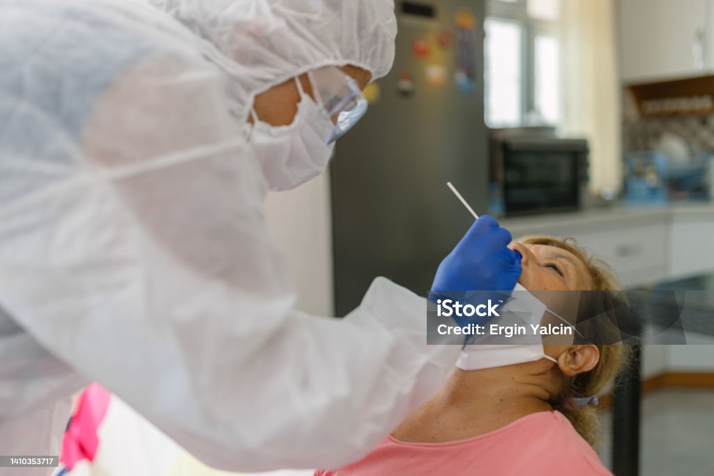 Doctor in protective workwear taking nose swab test from senior woman at home 70-79 Years Stock Photo