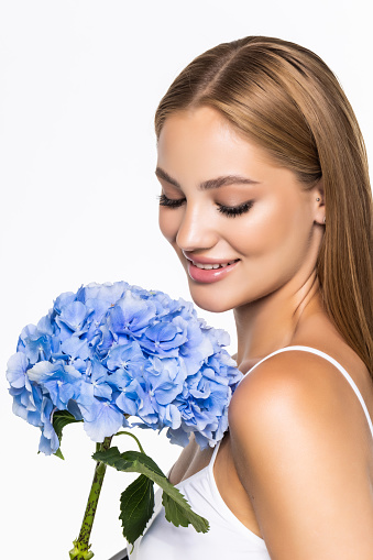 Beautiful young woman holding blue flower at face, isolated on white