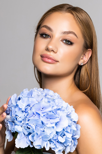 Beautiful young woman holding blue flower at face, isolated on white