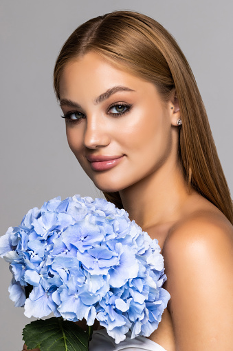 Young beautiful tanned woman with fresh make-up and gorgeous blue flower, over white background