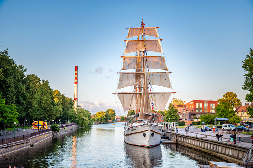 Klaipeda, Lithuania - August 08, 2019: Dane River promenade with tourists and the tall ship Meridianas in Klaipeda, Lithuania. The ship was built in 1948 in Finland as part of war reparations to the Soviet Union; today it is a restaurant and local landmark.