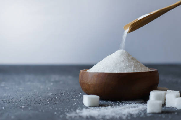 Heap of white granulated sugar in spoon and bowl with sugar cube